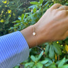 Woman wearing a 14k yellow gold cable chain bracelet featuring one 1/4” flat disc engraved with the letter L