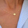 Woman with a 14k yellow gold cable chain necklace featuring one 1/4” flat disc engraved with the letter X