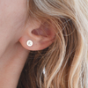 Woman wearing a 14k yellow gold stud earring featuring one 1/4” flat disc engraved with the letter E