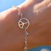 Woman wearing a Newport bracelet featuring one 1/2” cutout Peace Sign and 4 mm gemstones bezel set in 14k yellow gold