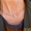 Woman wearing a Newport necklace featuring one 1/2” cutout Peace Sign and 4 mm gemstones bezel set in 14k yellow gold