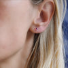 Woman wearing a Birthstone Stud Earring featuring a 4 mm briolette cut Ruby bezel set in 14k yellow gold