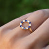 Hand with a Rosecliff small open circle ring featuring twelve alternating 2 mm sapphires and diamonds prong set in 14k gold