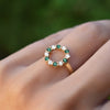 Hand with a Rosecliff small open circle ring featuring twelve alternating 2 mm emeralds and diamonds prong set in 14k gold