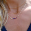Woman wearing multiple necklaces including a gold Rosecliff bar necklace with alternating 2 mm diamonds, rubies & sapphires