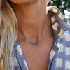Woman wearing a Rosecliff bar necklace with eleven alternating 2 mm round cut emeralds and sapphires prong set in 14k gold