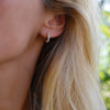 Woman wearing a Rosecliff huggie earring featuring 9 alternating 2 mm Nantucket blue topaz & diamonds prong set in 14k gold