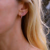 Woman wearing a Rosecliff huggie earring featuring nine alternating 2 mm rubies & diamonds prong set in 14k yellow gold