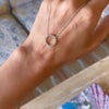 Hand holding a Rosecliff open circle necklace with sixteen 2 mm faceted round cut peridots prong set in 14k yellow gold