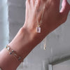 Braceleted woman's hand holding an Adelaide paper clip chain with a Warren emerald cut rose quartz pendant in 14k gold