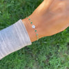 Woman with a Newport 14k gold bracelet featuring 4 mm briolette gemstones and a 1/4” flat disc engraved with the letter H