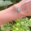 Woman wearing a Grand 1.17 mm cable chain bracelet in 14k yellow gold featuring one 6 mm briolette cut bezel set turquoise