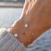 Woman wearing a 14k gold Classic bracelet featuring birthstones and one 1/4” flat disc engraved with a heart symbol