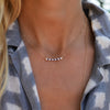Woman wearing a Rosecliff bar necklace with eleven alternating 2 mm round cut sapphires and diamonds prong set in 14k gold
