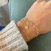 Woman wearing three bracelets including a 14k gold Noel bracelet featuring one 1/4” flat disc engraved with a snowflake