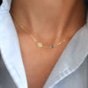 Woman wearing a 14k gold Solidarity necklace featuring one birthstone and one 1/4” flat disc engraved with a sunflower