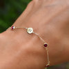 Woman wearing a 14k yellow gold Classic bracelet featuring rubies and one 1/4” flat disc engraved with the letter H