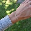Woman wearing a 14k gold Classic bracelet featuring two birthstones and one 1/4” flat disc, engraved with a four leaf clover