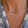 Woman wearing a Rosecliff bar necklace with eleven 2 mm faceted round cut alexandrites prong set in solid 14k yellow gold