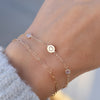 Woman wearing a 14k gold Classic bracelet featuring two birthstones and one 1/4” flat disc engraved with a heart symbol