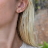 Close-up of a woman's ear wearing a Providence Garnet stud earring with a petite baguette stone set in 14k yellow gold