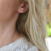 A woman's ear wearing a Providence Nantucket Blue Topaz stud earring with a petite baguette stone set in 14k yellow gold