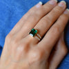 Woman's hand wearing a Warren ring in 14k gold with accent diamonds featuring one 10 x 8 mm emerald cut bezel set emerald