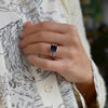 Woman's hand wearing a Warren ring in 14k gold with accent diamonds featuring one 10 x 8 mm emerald cut bezel set sapphire