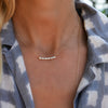 Woman wearing a Rosecliff bar necklace with eleven alternating 2 mm round cut alexandrites and diamonds prong set in 14k gold