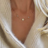 Woman wearing a 14k gold Classic necklace featuring four round birthstones and one 1/4” flat disc engraved with a heart