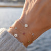 Woman with a 14k yellow gold Classic bracelet featuring two birthstones and one 1/4” flat disc engraved with a heart symbol