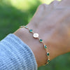 Woman with a Newport 14k gold bracelet featuring 4 mm briolette emeralds and a 1/4” flat disc engraved with the letter H