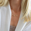 Woman wearing a 14k gold necklace featuring one 1/4” flat disc engraved with a heart symbol and two letter-engraved discs
