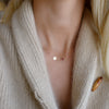 Woman wearing a 14k gold Classic necklace featuring one birthstone and one 1/4” flat disc engraved with a heart symbol