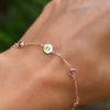Woman wearing a 14k gold Classic bracelet featuring pink tourmalines and one 1/4” flat disc engraved with the letter H