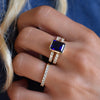 Woman's hand wearing a Rosecliff ring and a Warren ring in 14k gold with accent diamonds featuring one 10 x 8 mm sapphire
