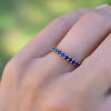 Hand wearing a Rosecliff stackable ring featuring eleven 2 mm faceted round cut sapphires prong set in 14k yellow gold