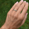 Hand wearing a Rosecliff stackable ring featuring eleven alternating 2 mm emeralds and diamonds prong set in 14k yellow gold