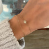 Woman wearing two bracelets including a 14k yellow gold Classic bracelet featuring one 1/4” flat disc engraved with a heart