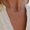 Woman wearing a Rosecliff bar necklace featuring eleven 2 mm faceted round cut amethysts prong set in 14k yellow gold