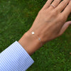 Woman's hand with a 14k gold Classic bracelet featuring one aquamarine and one 1/4” flat disc engraved with the letter H
