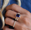 Woman's hand wearing a Rosecliff ring and a Warren ring in 14k gold with accent diamonds featuring one 10 x 8 mm sapphire