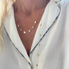 Woman wearing layered necklaces including a 14k yellow gold necklace featuring seven 1/4” flat discs engraved with letters