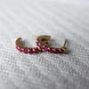 Two Rosecliff huggie earrings in 14k yellow gold each featuring nine 2mm faceted round cut prong set rubies