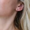 Close-up of a woman's ear wearing a Providence Alexandrite stud earring with a petite baguette stone set in 14k yellow gold