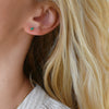 Close-up of a woman's ear wearing a Providence Emerald stud earring with a petite baguette stone set in 14k yellow gold