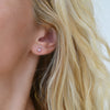 Close-up of a woman's ear wearing a Providence Amethyst stud earring with a petite baguette stone set in 14k yellow gold
