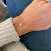 Woman wearing a 14k gold Classic bracelet featuring one birthstone and one 1/4” flat disc engraved with a heart symbol