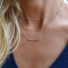 Woman wearing layered necklaces including a Rosecliff bar necklace with 2 mm round cut white topaz prong set in 14k gold