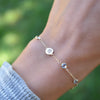 Woman wearing a 14k gold Classic bracelet featuring birthstones and one 1/4” flat disc, engraved with a four leaf clover